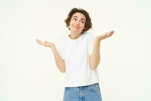 Portrait of brunette woman shrugging shoudlers, dont know, standing unaware, clueless, cant help, stands over white background photo