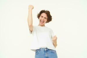 Portrait of happy, excited young woman winning, triumphing, feeling like champion, posing over white background photo