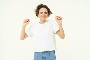 Portrait of happy smiling woman in wireless earphones, dancing and listening to music, enjoying her favourite song, posing over white background photo