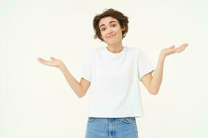 Woman shrugs her shoulders, looks clueless, doesnt know anything, stands confused against white background photo