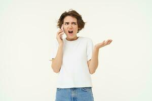 retrato de enojado dama hablando en teléfono, frustrado mujer gritos a su móvil teléfono, en pie terminado blanco antecedentes foto