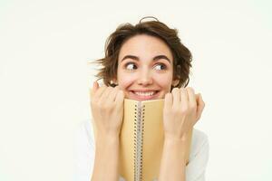 Portrait of happy woman with planner, holding notebook, reading notes and smiling, standing over white background photo