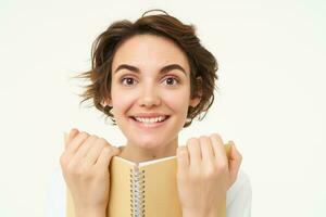 retrato de feliz, hermosa mujer participación planificador, haciendo notas, haciendo su tarea, en pie terminado blanco antecedentes foto