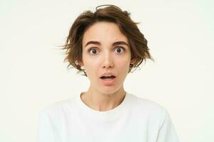 Close up shot of woman with shocked face, gasping and staring startled at camera, confused and surprised by something, standing over white background photo