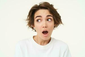 Close up shot of woman with shocked face, gasping and staring startled at camera, confused and surprised by something, standing over white background photo