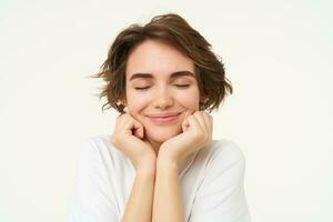 Close up of hopeful young woman, girl anticipating something, touching her face, looking forward to something, waiting with excitement, standing over white background photo