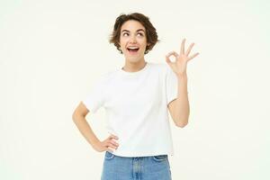 No problem, excellent. Young happy woman shows ok, okay gesture, nod in approval, recommending something good, standing over white background photo