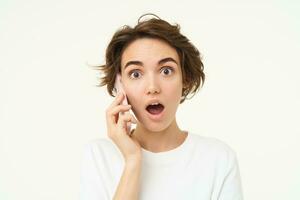Portrait of woman with surprised face, answers phone call and looks excited, amazed by big news, stands over white background photo