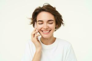 Image of smiling, brunette woman calling someone, talking on mobile phone, answer telephone call, standing over white background photo