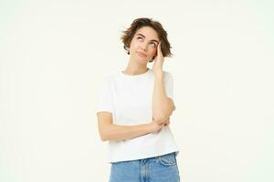 Portrait of puzzled woman, looking confused, staring up at ceiling, touches her head, standing tired against white background photo