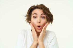 Portrait of girl with surprised face, makes shocked expression, stands over white background photo