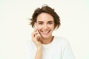 imagen de linda morena mujer responder teléfono llamar, hablando en teléfono inteligente, participación móvil cerca comer y sonriente , en pie terminado blanco antecedentes foto