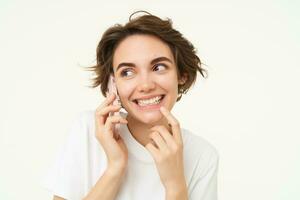 Image of smiling, brunette woman calling someone, talking on mobile phone, answer telephone call, standing over white background photo