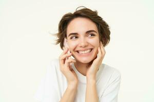 Portrait of happy, chatty young woman talking on mobile phone, using smartphone, calling someone, standing over white studio background photo