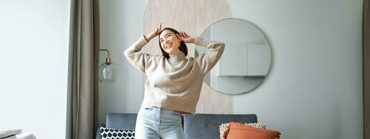 Joyful young korean woman dancing, raising hands up and looking upbeat, feeling healthy and upbeat photo