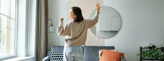 Beautiful asian woman dancing, feeling happy and upbeat, singing into hand microphone, express joy, positivity and happiness photo