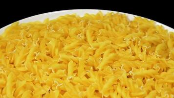 ungekocht Fusilli Pasta auf Weiß Teller rotierend gegen schwarz Hintergrund. Fett und ungesund Lebensmittel. trocken Spiral- Makkaroni. Italienisch Kultur und Küche. roh golden Pasta video