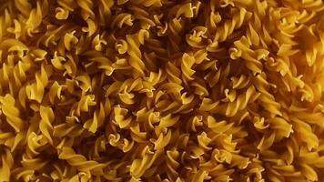 okokt fusilli pasta topp se, låg nyckel ljus. fett och ohälsosam mat. torr spiral makaroner, roterande bakgrund. italiensk kultur och kök. rå gyllene pasta mönster. vänster rotation video