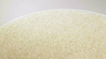 seco cru branco arroz em branco prato rotativo contra branco fundo. espalhados cru grandes grão arroz. ásia cozinha e cultura. saudável comendo ingredientes. dieta Comida video