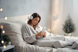 ai generado un joven mujer en gris ropa y auriculares mentiras en cama y escucha a música, un audio libro o relojes un película. Navidad atmósfera foto
