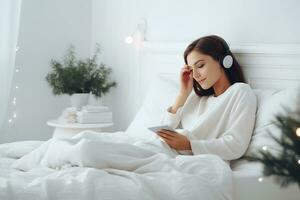 ai generado un joven mujer en blanco ropa y auriculares mentiras en cama y escucha a música, un audio libro o relojes un película. Navidad atmósfera foto