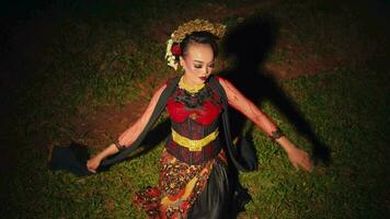 an Asian woman is sitting on a green grass while dancing with her hands and a red scarf in a forest video