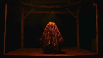un mujer en un batik Pañuelo es sentado en un misterioso choza mientras ejecutando un ritual video