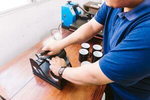 Hands of an unrecognizable man holding a sublimation machine designs on a mug. photo