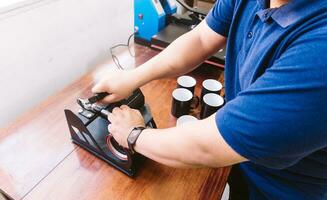 Hands of an unrecognizable man holding a sublimation machine designs on a mug. photo