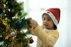 Children kids girl hanging a small glitter ball decorating christmas tree for celebrate christmas and new year party at home. Preparing for holiday. Happiness Christmas day. Have fun. X-mas concept. photo