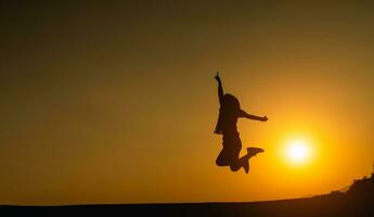 Silhouette of woman jumping and success for goal target on the field lawn with beautiful sunset sun light background for web banner and advertisement. photo