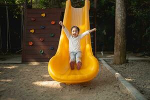 Cute asian girl smile play on school or kindergarten yard or playground. Healthy summer activity for children. Little asian girl climbing outdoors at playground. Child playing on outdoor playground. photo