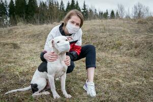 A young girl and a dog in medical masks play in nature. photo