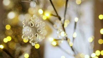 Close up snowflake toy hanging on the christmas tree, on New Year Eve in cozy house with atmosphere of magic in air. Background bokeh of side flickering light bulbs garlands video