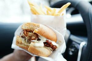 Asian woman driver hold and eat hamburger in car, dangerous and risk an accident. photo