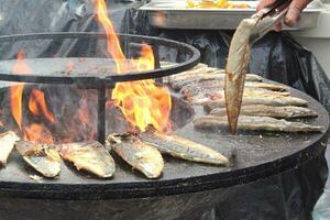 A la parrilla pescado en un en forma de cuenco plano parrilla con fuego agujero en el centro. al aire libre Mariscos parilla cocinando. picnic en patio interior en abierto aire. calle comida concepto. preparando pescado terminado abierto hoguera foto