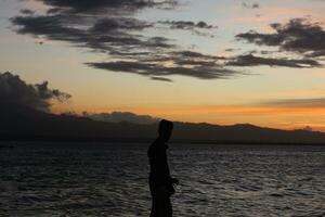 Silhouette of a young man standing by the lake enjoying the sunset. peaceful atmosphere in nature photo