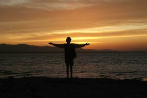 silueta de un joven parado junto al lago disfrutando de la puesta de sol. ambiente tranquilo en la naturaleza foto