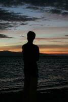 Silhouette of a young man standing by the lake enjoying the sunset. peaceful atmosphere in nature photo