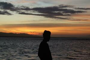 silueta de un joven parado junto al lago disfrutando de la puesta de sol. ambiente tranquilo en la naturaleza foto