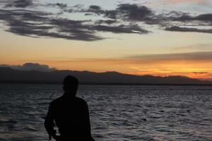 Silhouette of a young man standing by the lake enjoying the sunset. peaceful atmosphere in nature photo