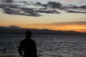 silueta de un joven parado junto al lago disfrutando de la puesta de sol. ambiente tranquilo en la naturaleza foto