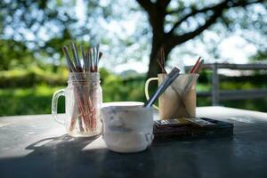 Paint brushes in glass jar on wooden table in the garden for preparing to paint pottery. photo