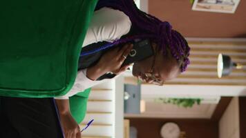 Vertical video Worker managing bookings by phone, answering calls to register to clients for room reservation and writing personal information on clipboard. Hotel staff taking notes using telephone line.