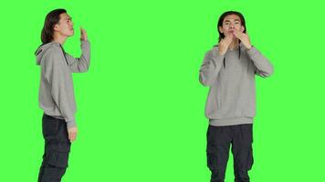 Asian man sending air kisses in studio, acting romantic and sweet standing against greenscreen backdrop. Young person feeling confident and flirty showing true lovely emotions. video