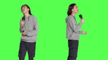 Trendy guy performs karaoke on camera, using recording device to sing popular melodies and lyrical content. Young man having an excellent time over greenscreen backdrop, creating sounds and songs. video