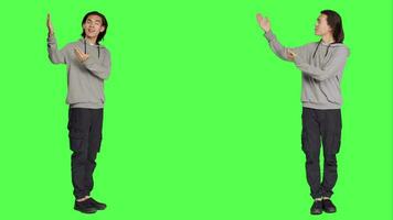 Asian person works on marketing ad in studio, pointing to left or right sides for new advertisement campaign. Young male model smiling and working on commercial, standing over greenscreen. video