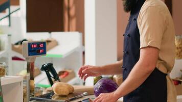 Mann im Schürze Überprüfung Gewicht von Produkte mit modern Supermarkt Rahmen und verkaufen frisch Essen zu Kunde. lokal Lebensmittelgeschäft Geschäft Inhaber Gewichtung Kartoffeln und Pasta im wiederverwendbar Krug. Handheld Schuss. video