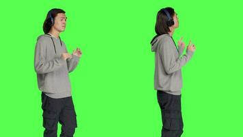 Energetic adult does jazzy moves in studio while he enjoys popular tracks. Asian modern person smiling and bouncing on camera, listening to funky music with audio headset. video