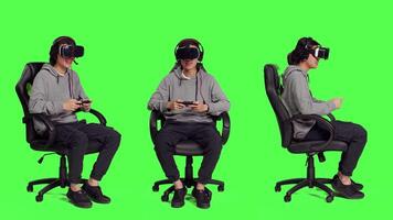 Person rests on chair over greenscreen backdrop and performs video games using virtual reality eyewear and mobile device, takes part in online multiplayer contest. Asian guy loving combat games.